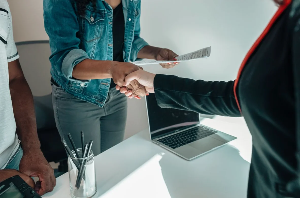 Two people shaking hands over a contract at an office desk